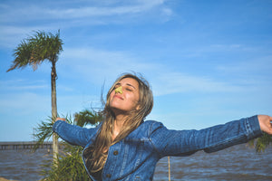 Girl wearing neon yellow vegan and environmentally friendly Nöz sunscreen in the summer in front of a beach wearing a denim jacket